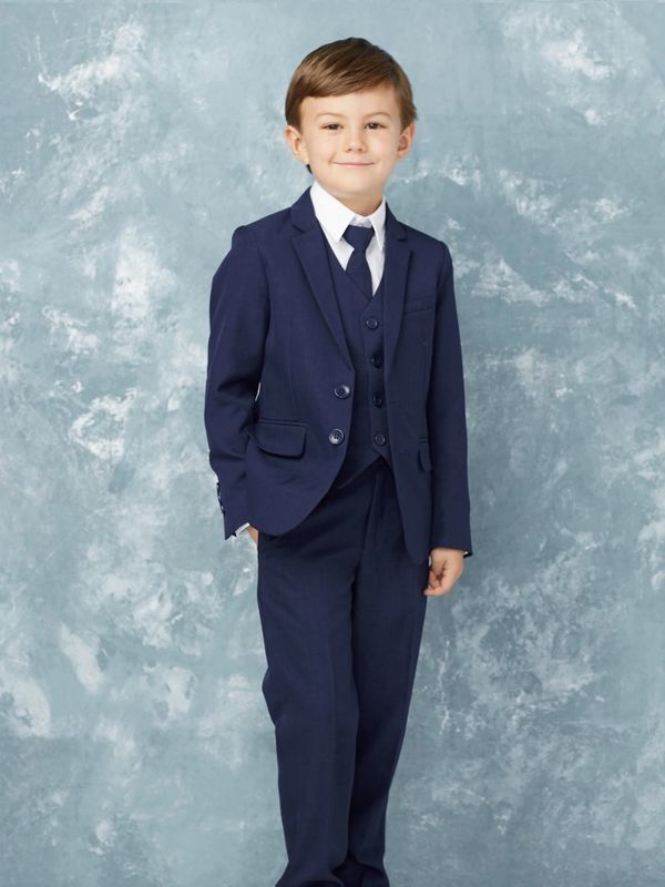 Young boy dressed in a navy blue suit with a tie, standing confidently.