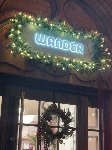 Illuminated sign reading 'WANDER' decorated with festive greenery and lights.