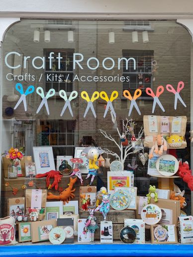 Colorful craft store window with kits, accessories, and handmade stuffed animals.