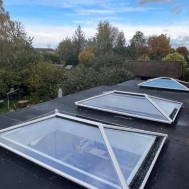 Three triangular skylights on a flat roof overlooking trees and a blue sky.