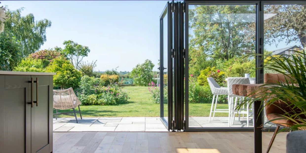 Open glass doors lead to a lush garden with outdoor seating.