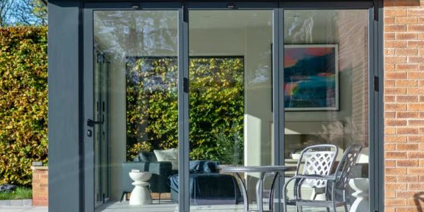 Modern glass doors open to a cozy living room with outdoor seating.