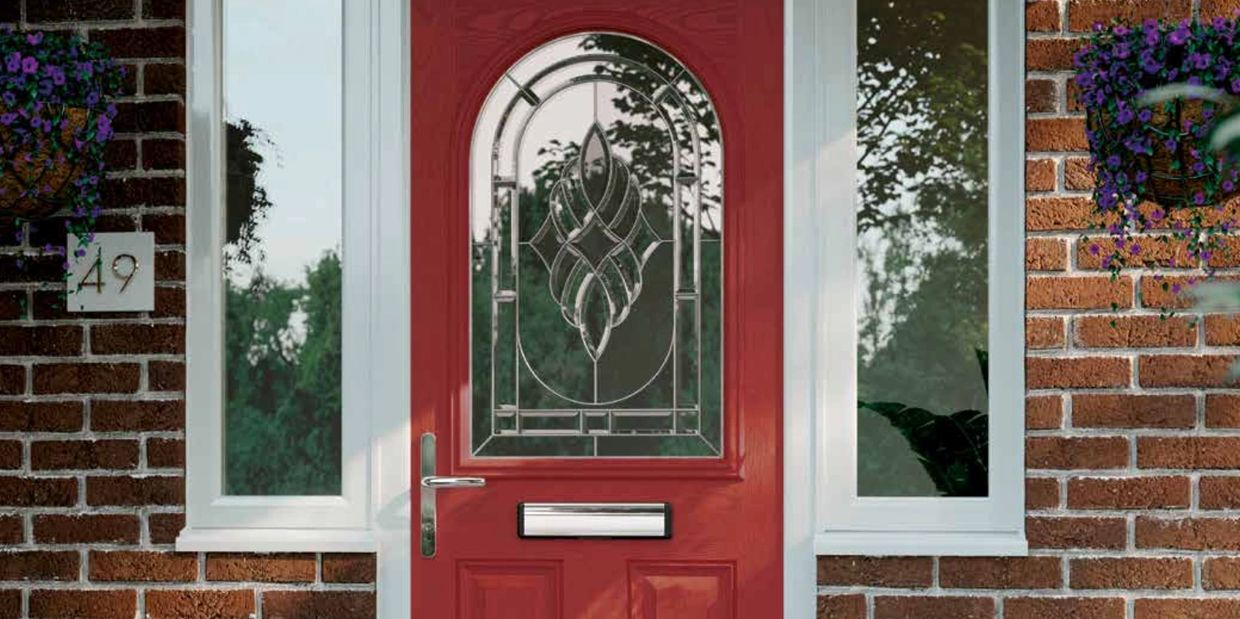 Red front door with decorative glass panels on a brick house.