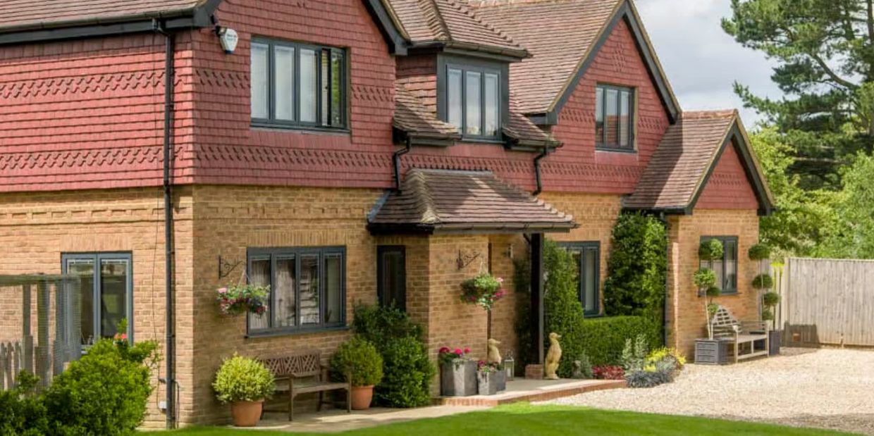 A charming brick and red-tiled house with a well-kept garden and greenery.