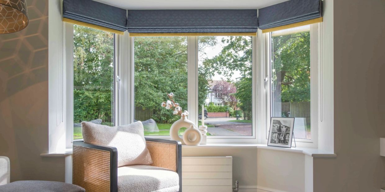 Cozy corner with cushioned chair by a large bay window and decorative vases.
