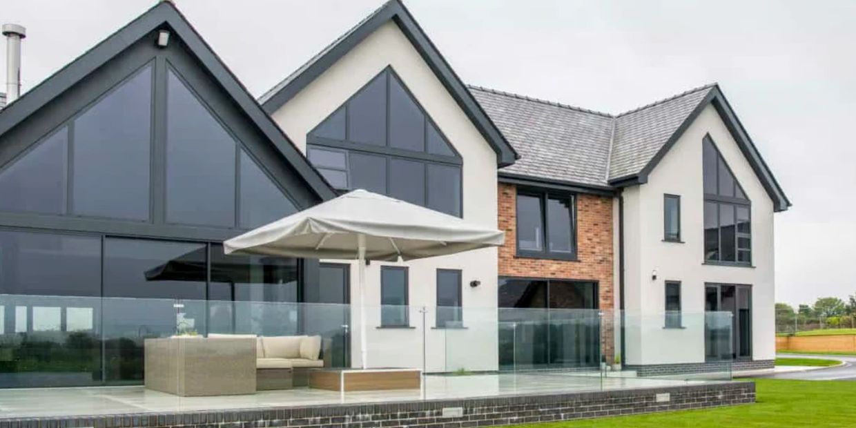 Modern house with large windows and outdoor seating under an umbrella.