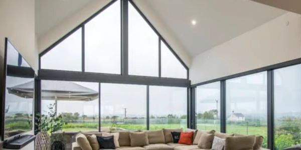 Modern living room with large triangular windows and beige sectional sofa.