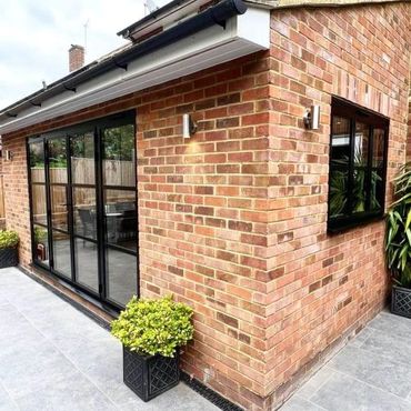 Modern brick house extension with large black-framed glass doors and potted plants.