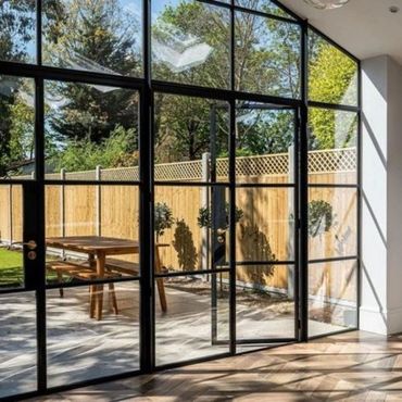 Modern glass doors open to a sunny backyard with a wooden table and fence.