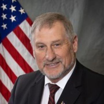 Portrait of a man in a suit with an American flag background.
