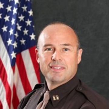 Portrait of a uniformed officer in front of an American flag.