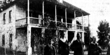 Black and white photo of four people standing in front of a large two-story house.