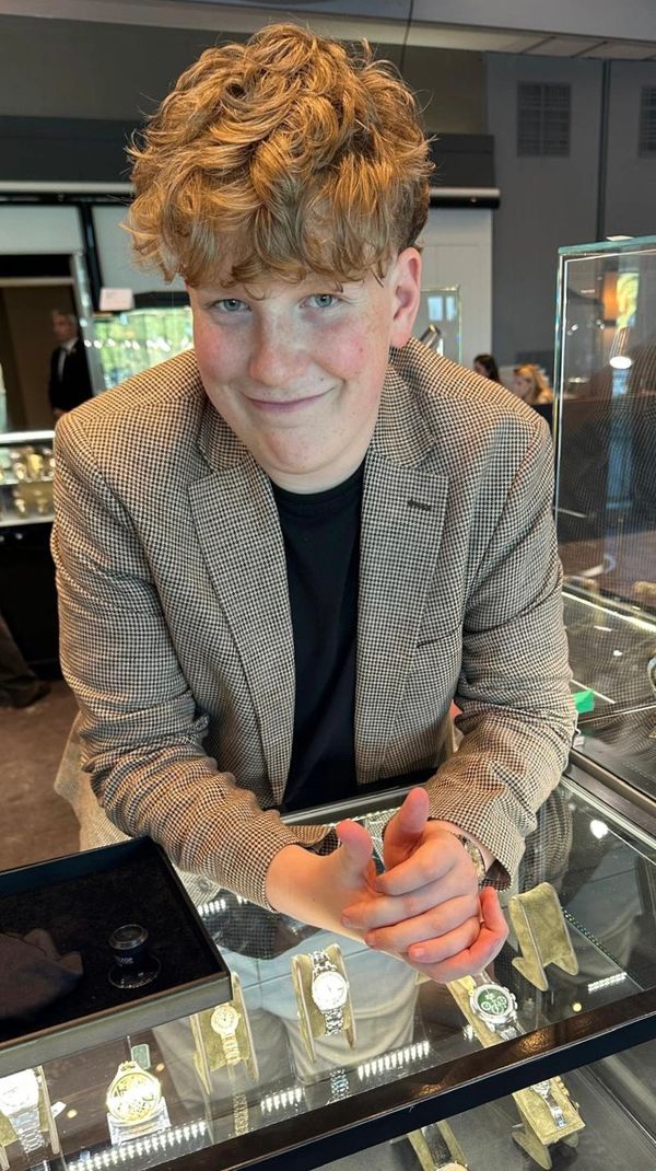 Young man smiling behind a glass display of luxury watches.