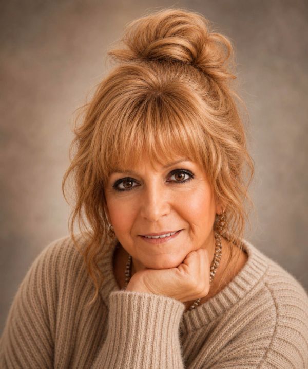 Smiling woman with light brown hair in a cozy beige sweater.