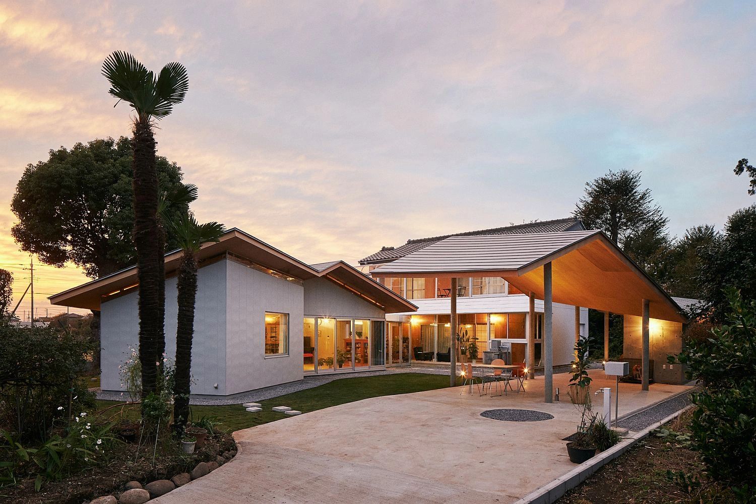 Modern house with angled roofs and warm lighting at sunset.
