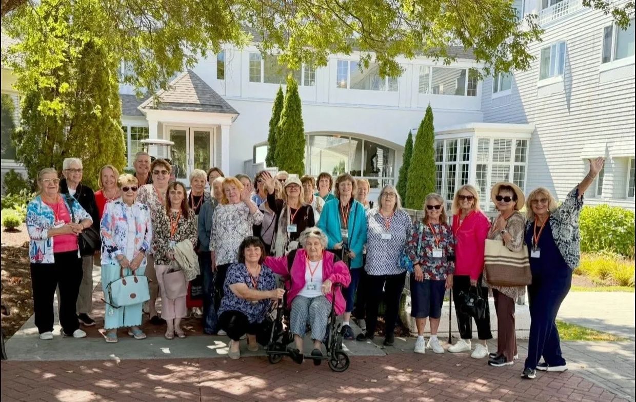 Group of elderly women posing outside a white building under a tree.