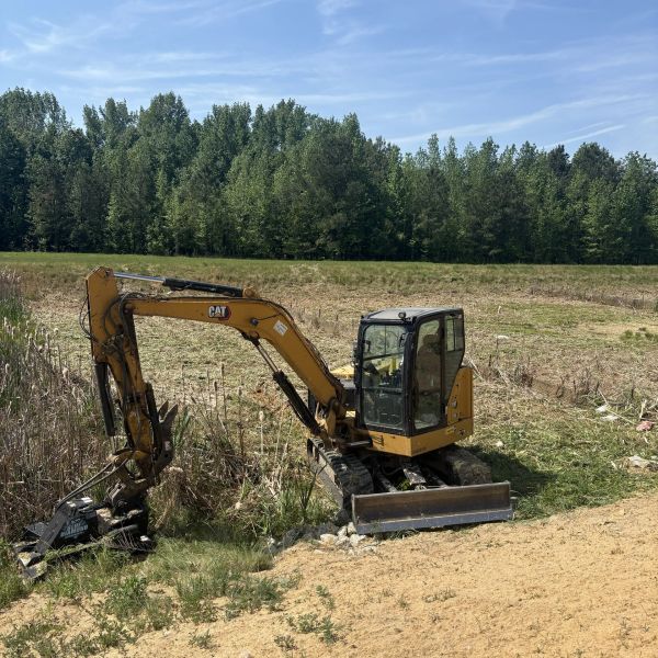 Yellow excavator working near a grassy field.