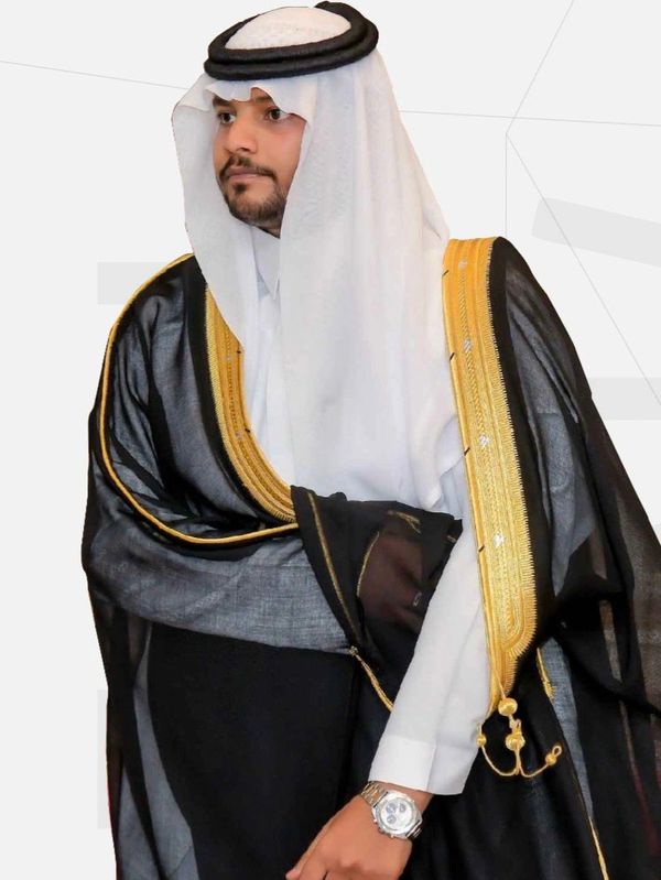 Man in traditional Middle Eastern attire with a black and gold bisht and white ghutra.