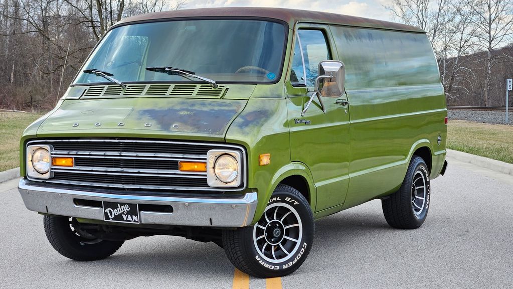 Vintage green Dodge van parked on a road with a rustic look.