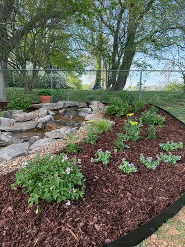 A landscaped garden bed with blooming flowers and a small rock water feature.