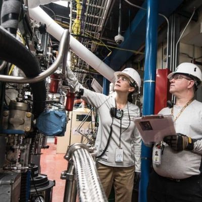 Two engineers in hard hats inspecting industrial machinery in a plant.