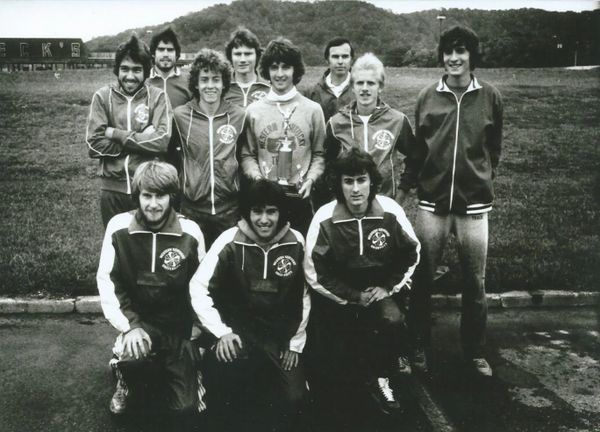 Black and white photo of a men's sports team posing outdoors with a trophy.