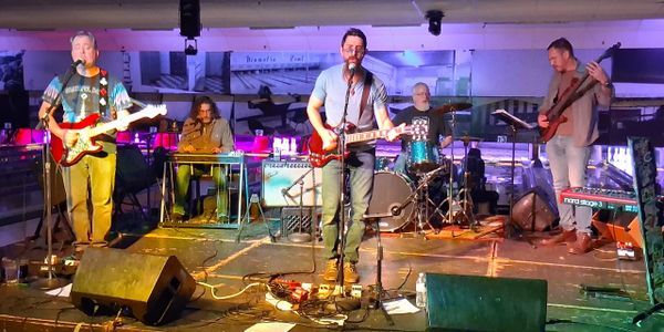 Five musicians performing live on stage with guitars and drums under colorful lighting.