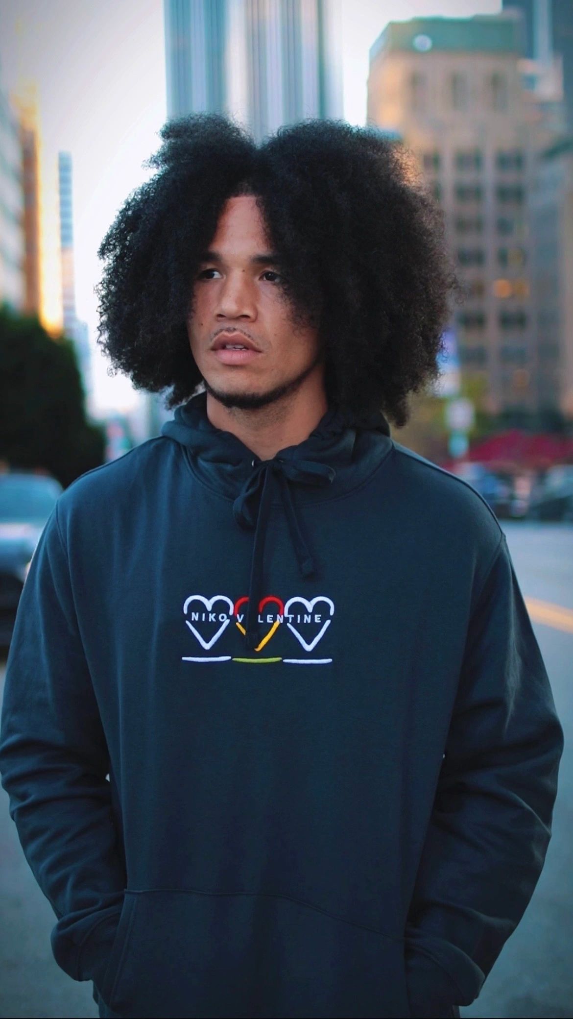 Young man with afro hair wearing a black hoodie in an urban setting.