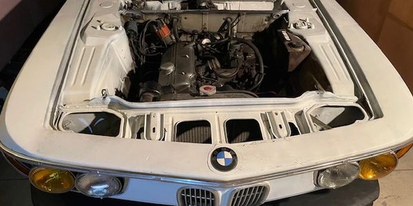 Vintage white BMW car with its hood open showing the engine.