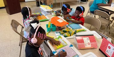 Children wearing headphones working on school assignments at a table.