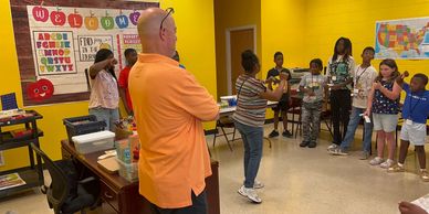 Teacher watches students presenting in a bright classroom.
