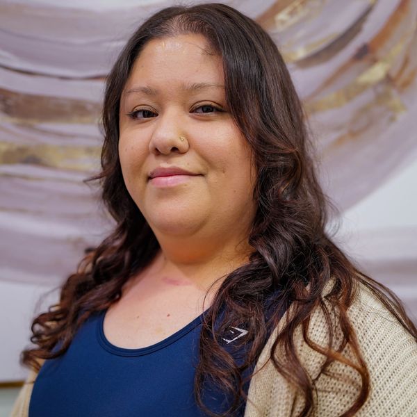 Smiling woman with long curly hair wearing a blue top and beige cardigan.
