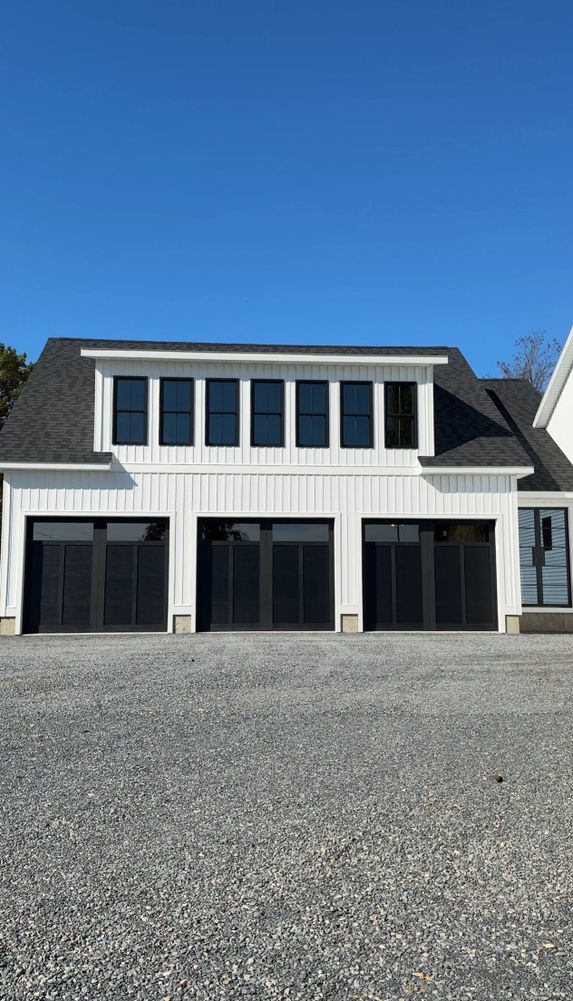 Modern white garage with black doors and multiple windows under a clear blue sky.