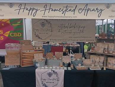 A market stall showcasing honey and beeswax products from Happy Homestead Apiary.