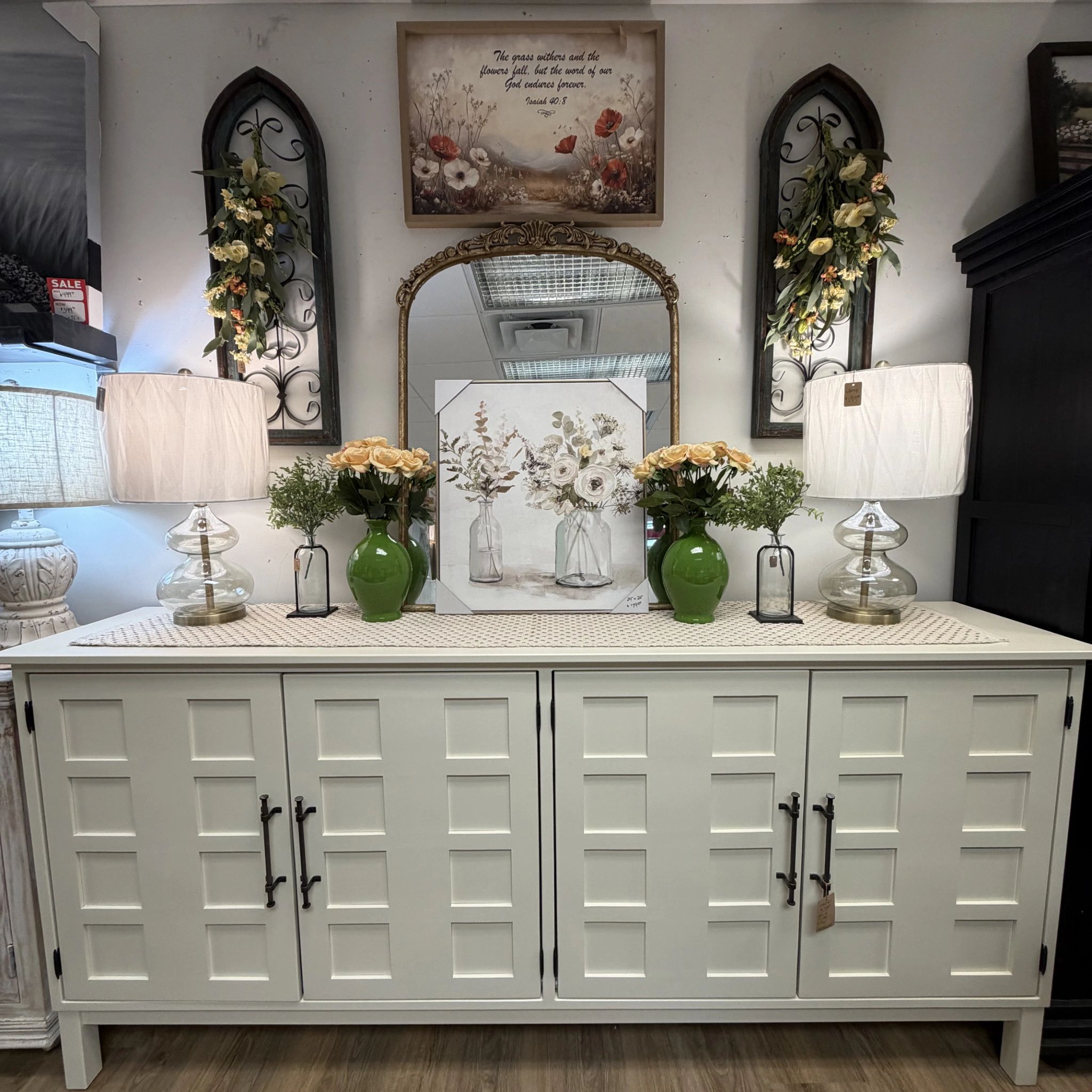 Decorative cabinet setup with lamps, flowers, and a mirror.