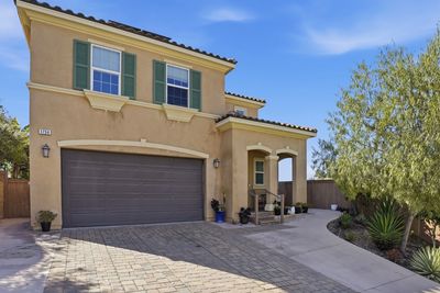 Two-story beige house with green shutters and a paved driveway.
