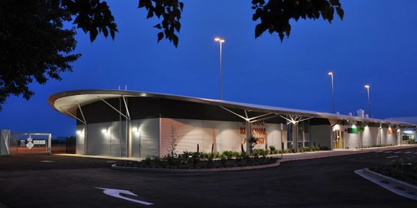 Modern airport terminal building illuminated at dusk with clear blue sky.