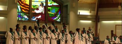 Choir singing in a church with stained glass background.