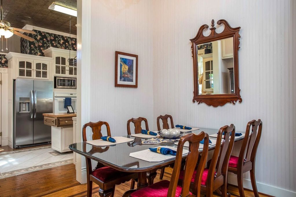 The large dining table and glass-enclosed hutch with several vintage plates, pictures, and ceramics.