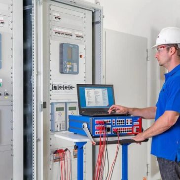 Technician testing electrical equipment with laptop and measuring devices.