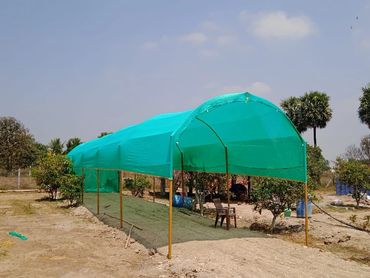 Green shade net structure in a garden area under blue sky.