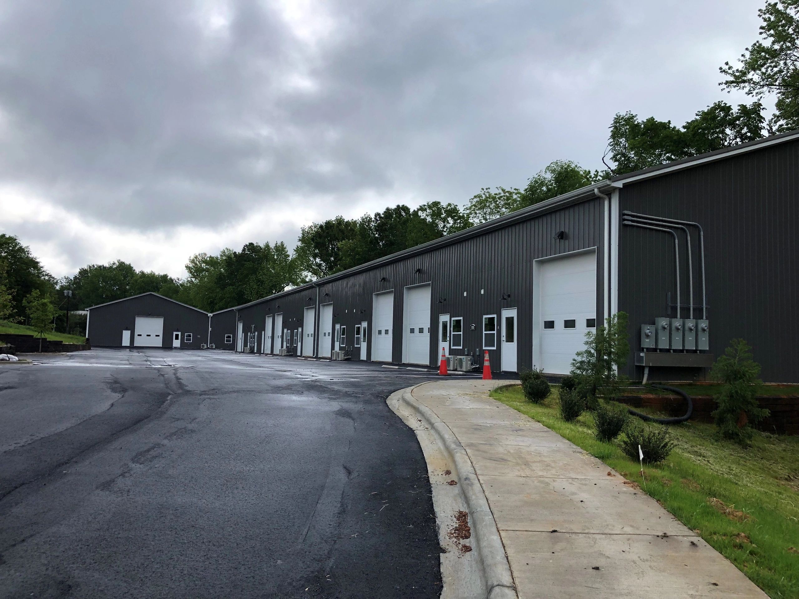 Row of dark industrial buildings under cloudy sky.