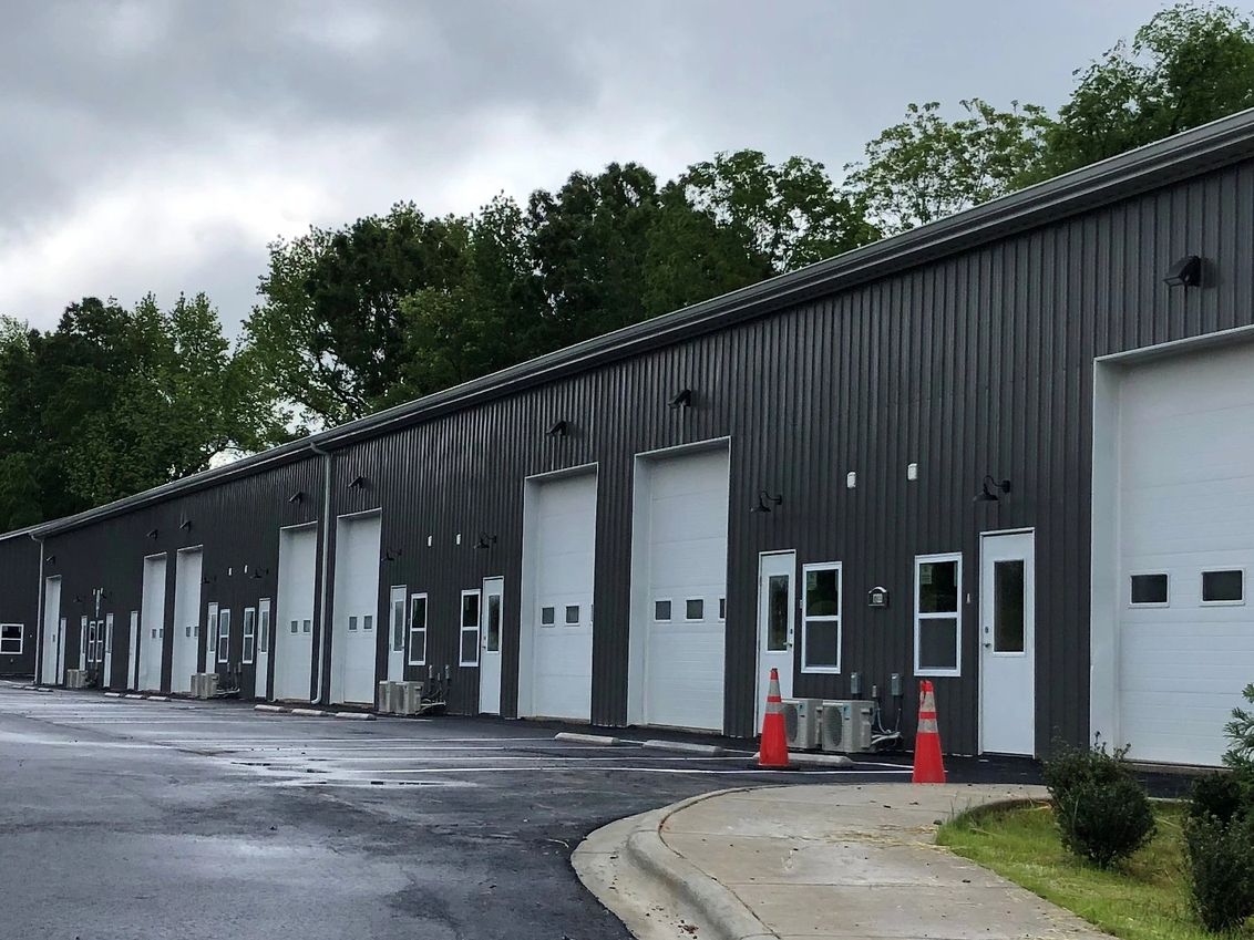 Row of dark industrial buildings under cloudy sky.