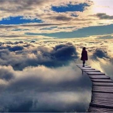 Person standing at the edge of a wooden path above the clouds.