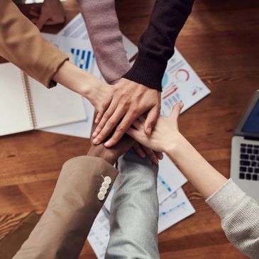 Diverse team joining hands in a unity gesture over office documents and laptop.
