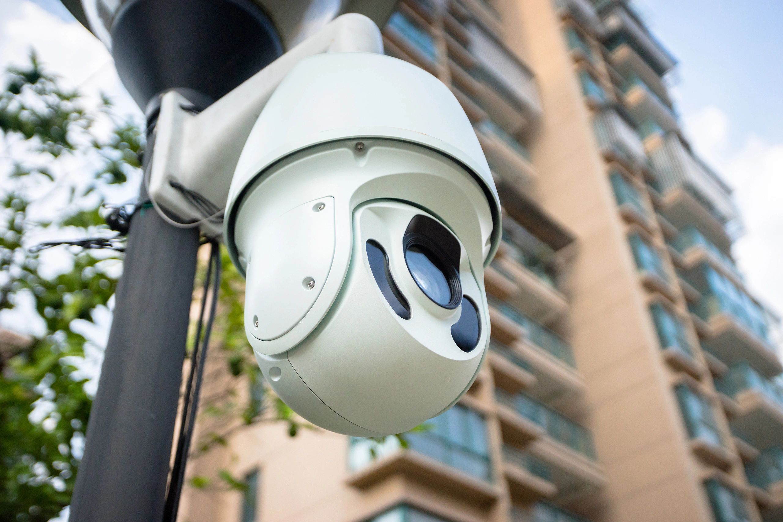 White PTZ camera mounted to a light pole overlooking a hotel parking lot 