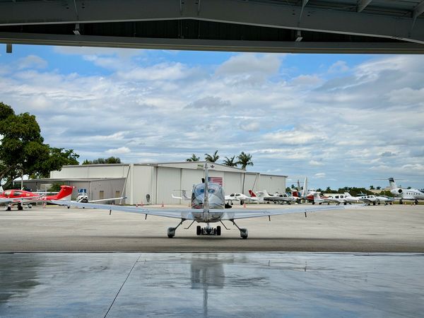 Small airplane parked in a hangar with other aircraft outside.