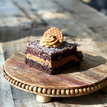 A decadent chocolate brownie with peanut butter frosting and a waffle cookie on top.
