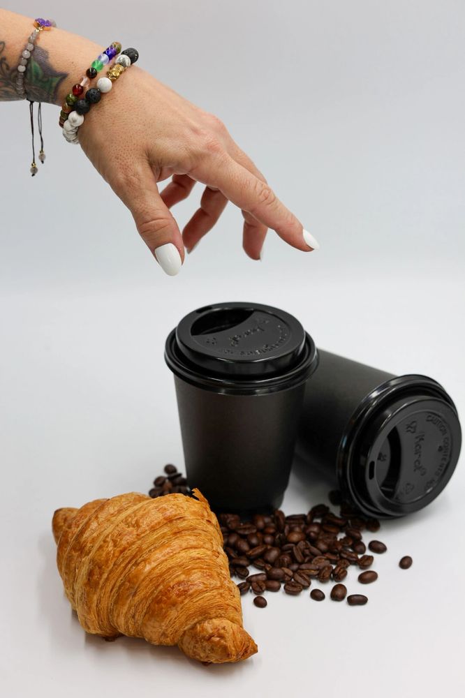 Hand reaching for black coffee cup with a fresh croissant and whole beans spilled nearby