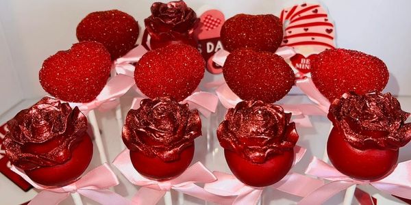 Valentine-themed cake pops with red hearts and roses decorated with pink bows.